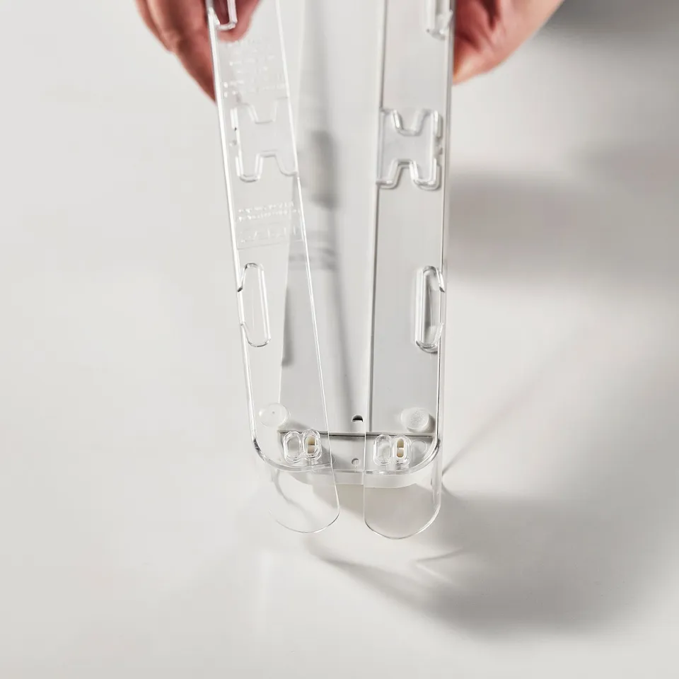 Hand holding transparent drink holder, adjustable to organise cans/bottles in fridge, shown with h-shaped connector slots.