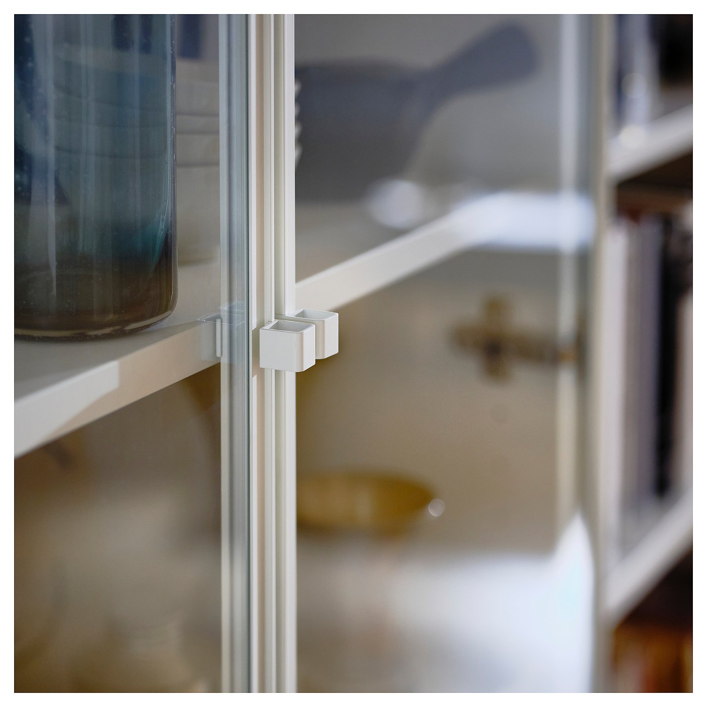 Close-up of HÖGBO glass doors white hinge. Modern, metallic, clean-lined design.