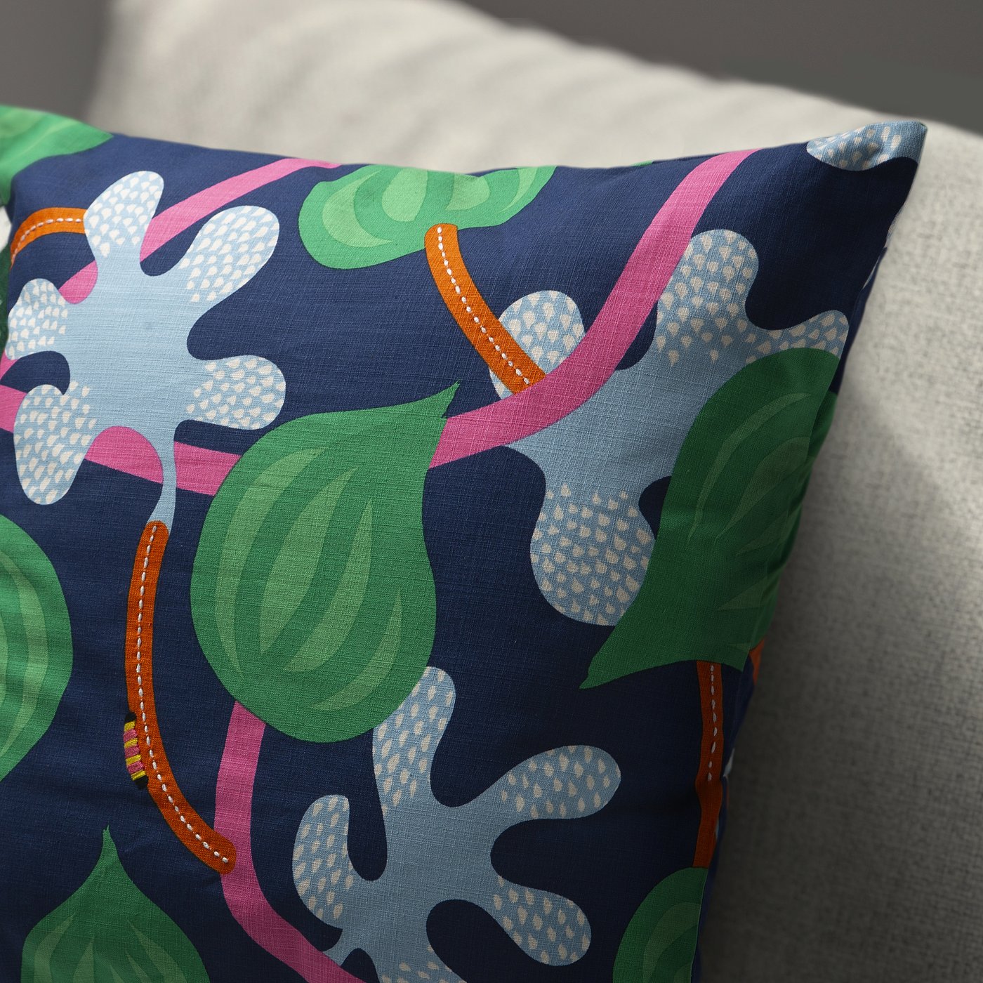 Colourful cushion cover with abstract leaf patterns and playful hand-embroidered caterpillar on navy blue fabric.