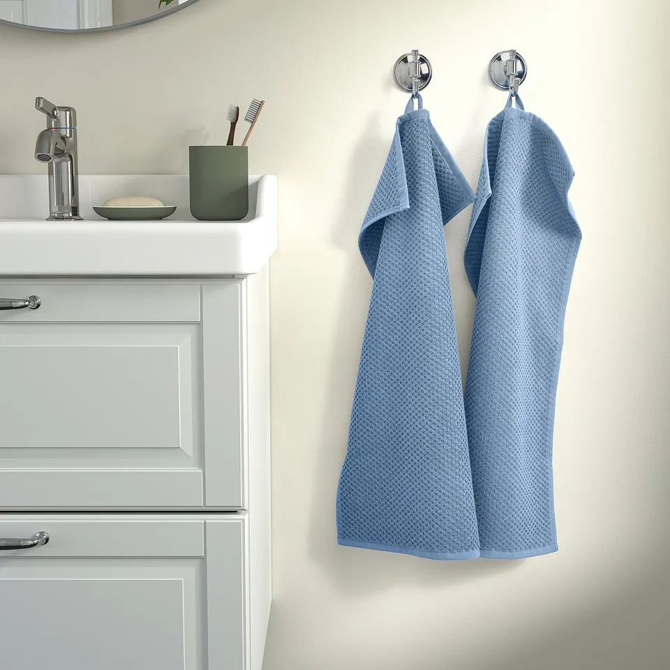 Blue towels hang on hooks by white vanity with green holder.