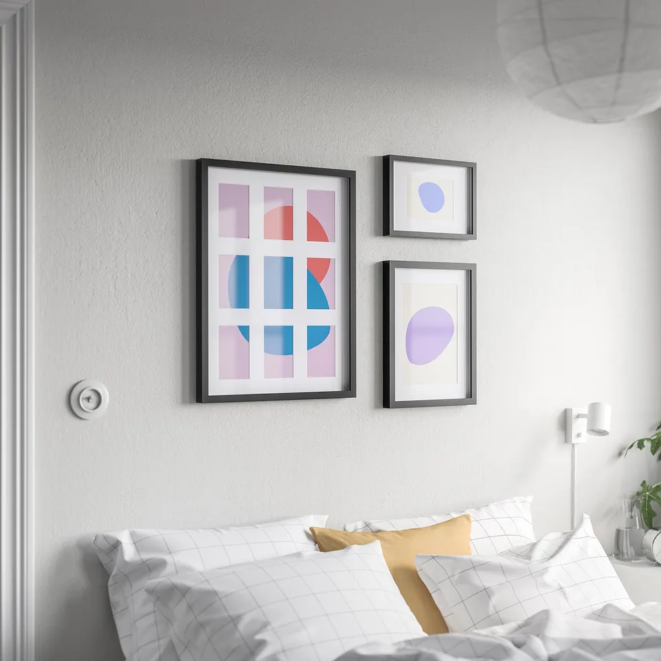 Three modern RÖDALM frames with colourful prints above a bed with white grid comforter.