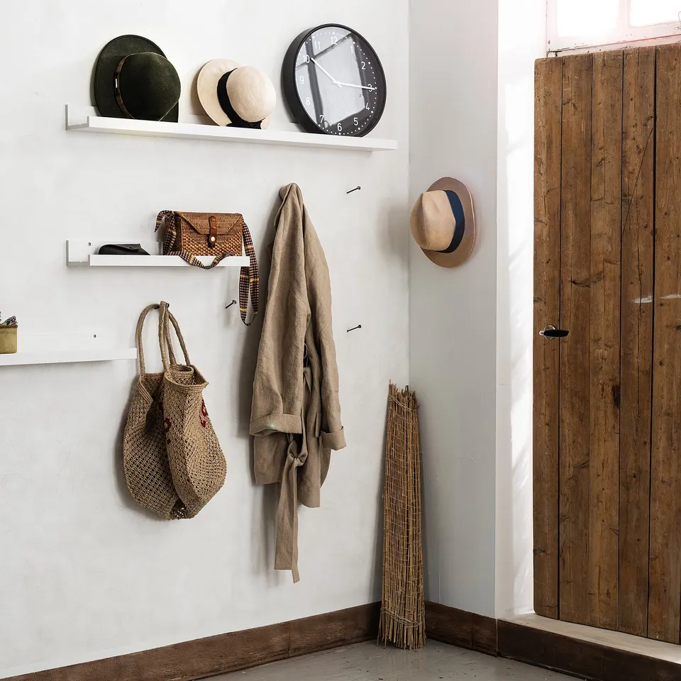 Shelves hold hats, bags, clock. Coat hangs beside tools. Door on right.