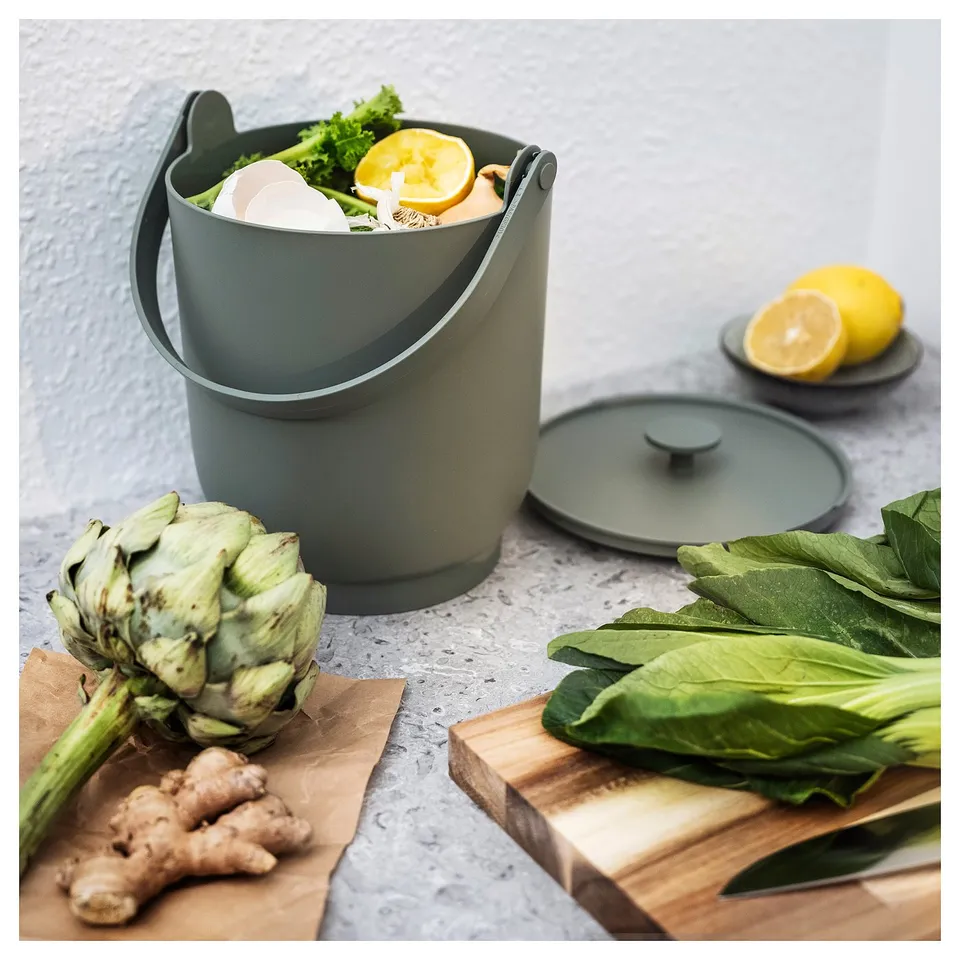Grey compost bin with veggies on kitchen counter.
