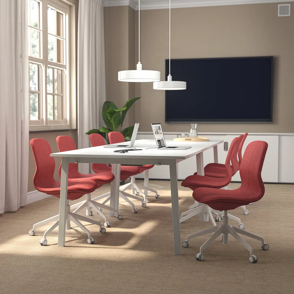 Modern conference setup with white table, red chairs, pendant lights, large tv.