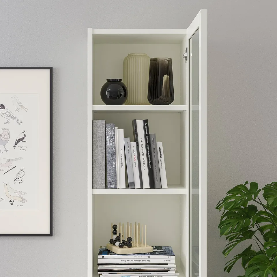 White BILLY bookcase with glass doors, displaying books, decorative vases, and a plant.