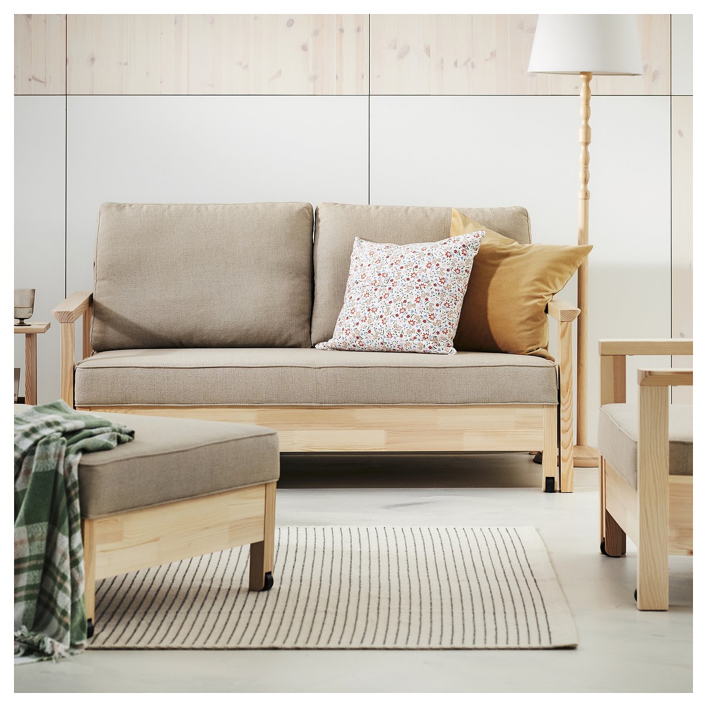 Minimalist living room with light grey sofa, wooden sides, and two pillows. Stripes rug beneath, lamp on the right.