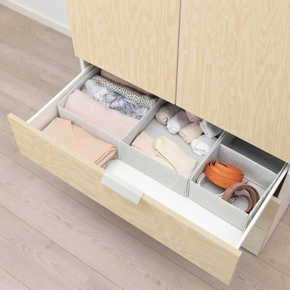Wooden drawer organiser with compartments holding folded clothes and accessories in a neat, structured manner.
