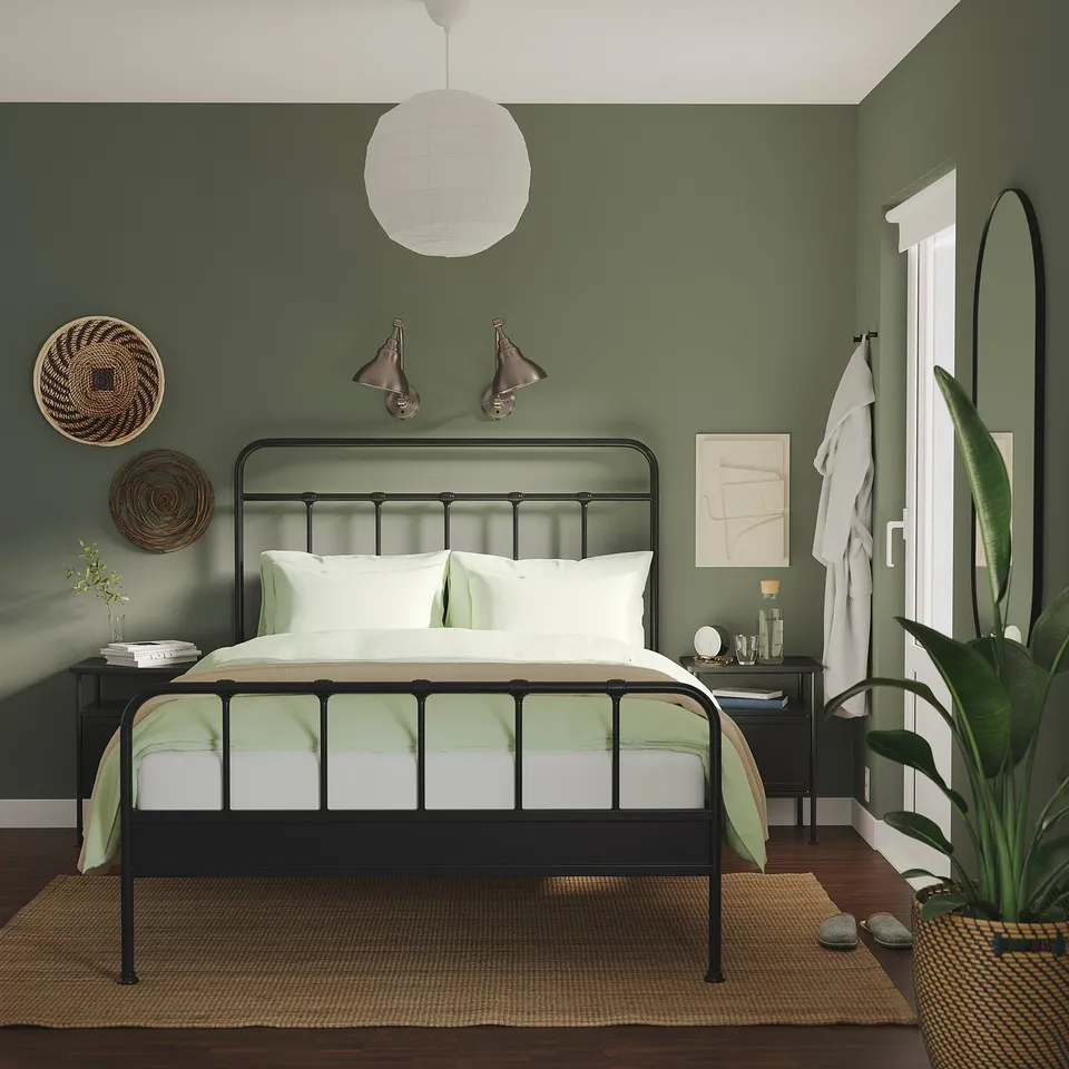 Black STJÄRNÖ bed, green walls, round lantern, green bedspread, nightstands with lamps, books, plants, mirror, houseplant.