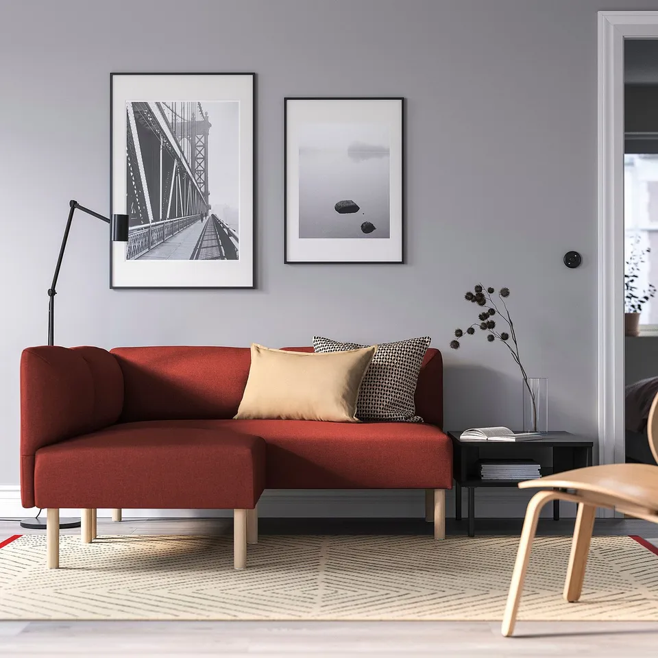 Modern living room: red lillem modular sofa with geometric rug, grey walls, black lamp, framed photos, side table, and a wooden chair.