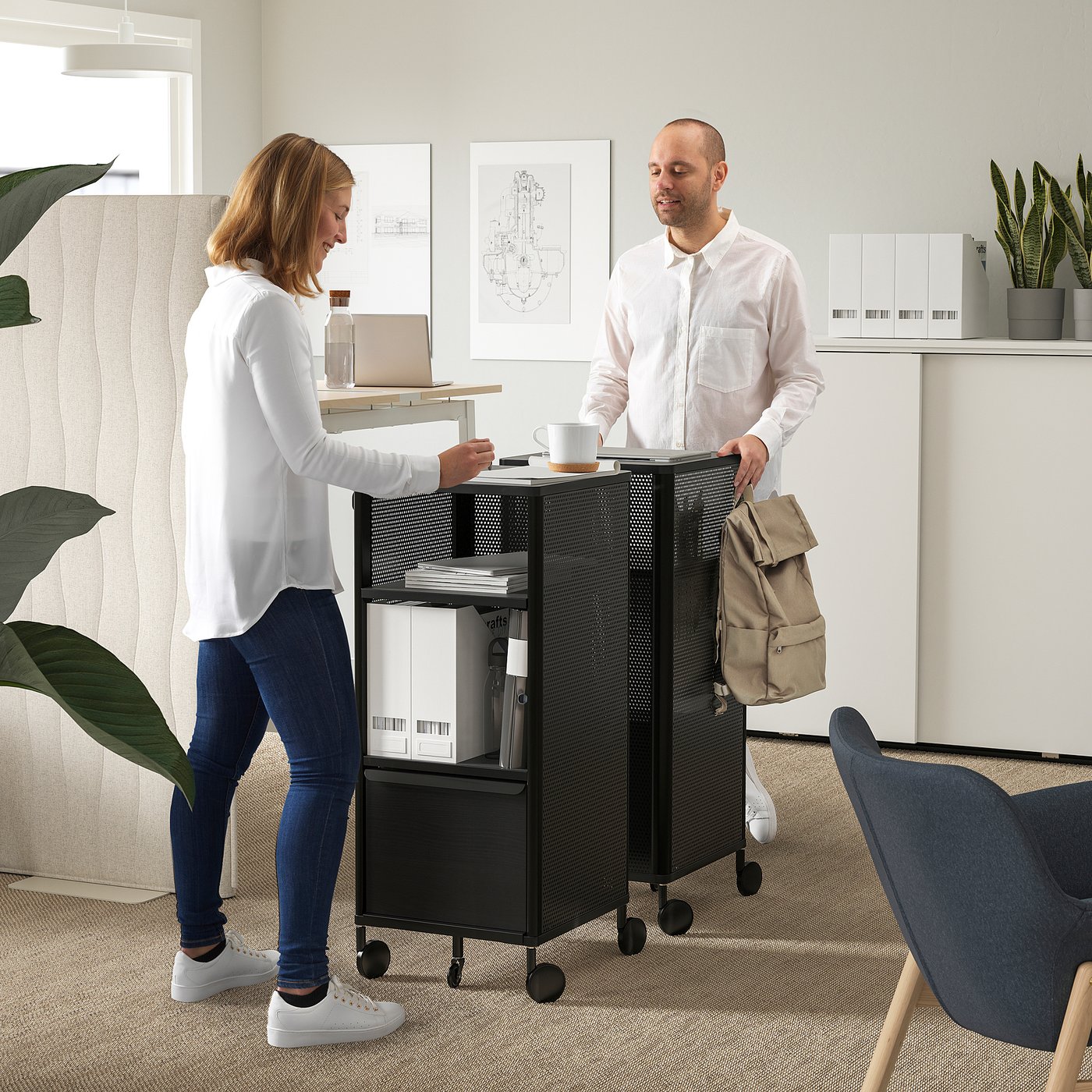Two people near a BEKANT cart: one hands over papers, showcasing its use as a portable workspace with adjustable shelves.