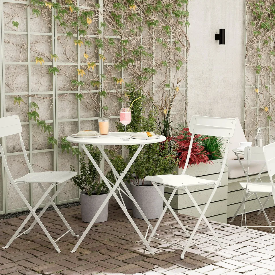 Cosy outdoor café setup with white SUNDSÖ table and chairs, greenery, plates, and glasses.