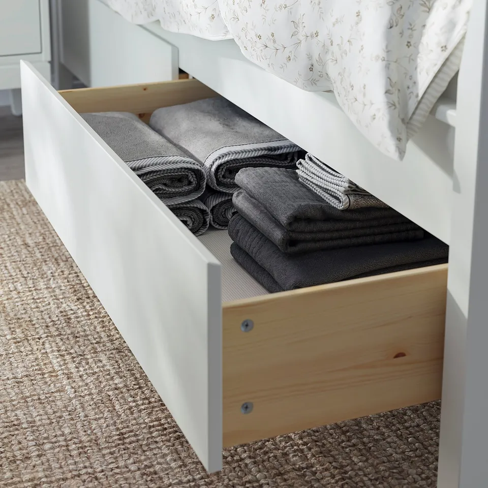 White IDANÄS bed with open storage drawer filled with folded grey towels.
