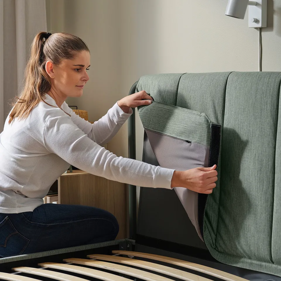 A person adjusts a TÄLLÅSEN bed frame with removable upholstery and slats.