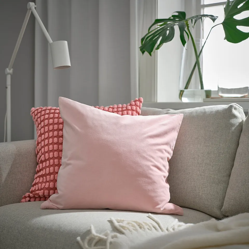 Living room corner with grey couch, SANELA pillow, patterned pillow, fringed throw, and green plant.
