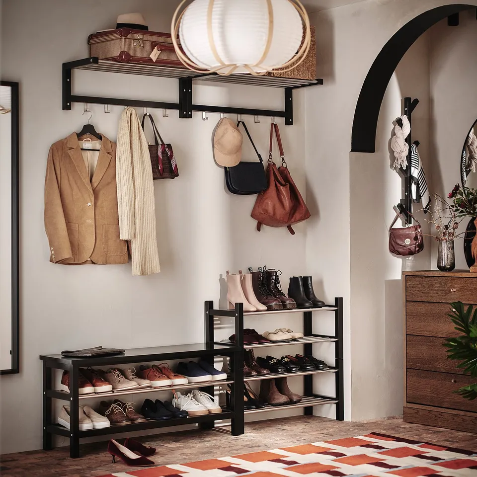 Entryway with TJUSIG shoe rack, jackets, and bags. Wood and metal design against a white wall with an arched doorway.