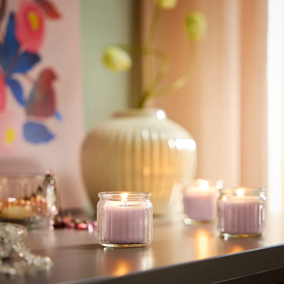 Shelf with 3 small lit candles, vase, and painting.