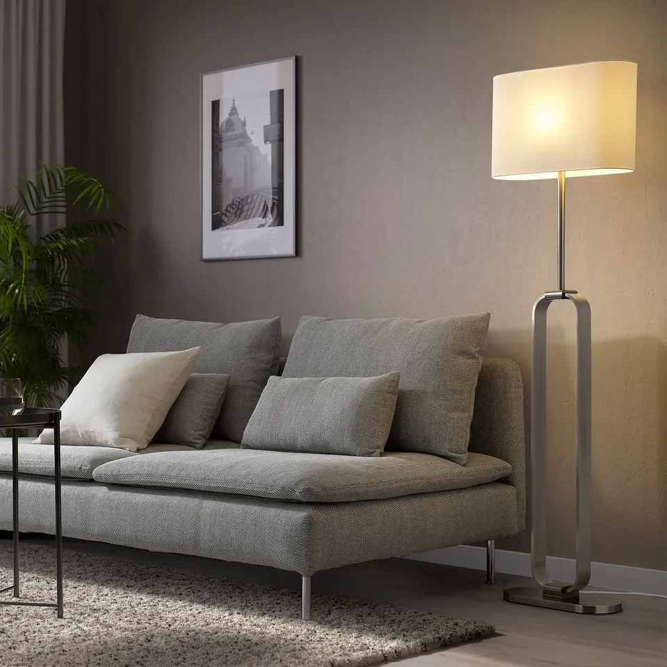 A modern living room with UPPVIND gold floor lamp beside a grey sofa, featuring patterned cushions and a black-and-white framed wall picture.