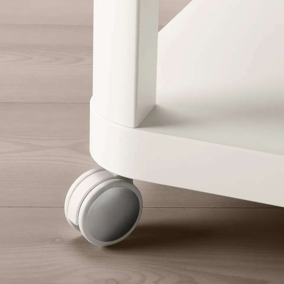 Close-up of a white rolling table leg with grey castor wheel on beige wooden floor.