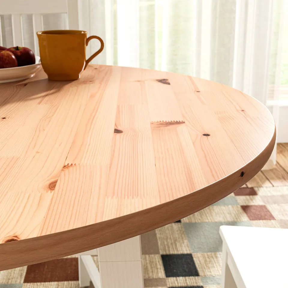 Light wooden round table with smooth edges, a yellow mug on top, near a window with sheer curtains.