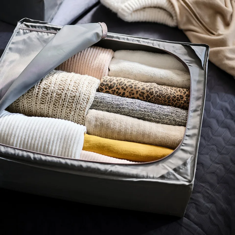 Folded sweaters organised in a clear, portable SKUBB storage case with handle, suitable for under-bed or wardrobe use.