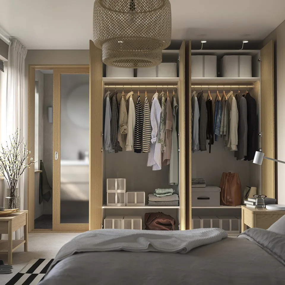 Bedroom with open wardrobe displaying clothes, shelves, and storage boxes. Light fixture hangs above, reflecting modern organisation.