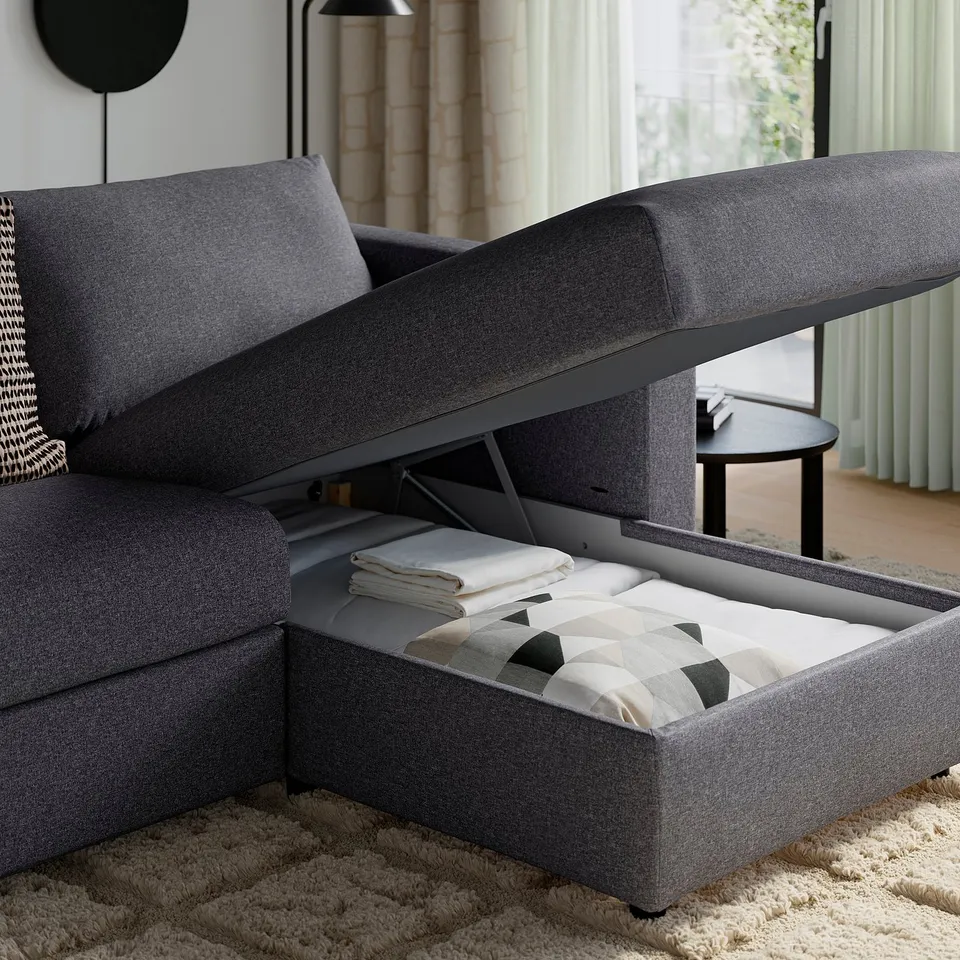 A VIMLE sofa with a lifted chaise longue revealing storage underneath, filled with blankets.