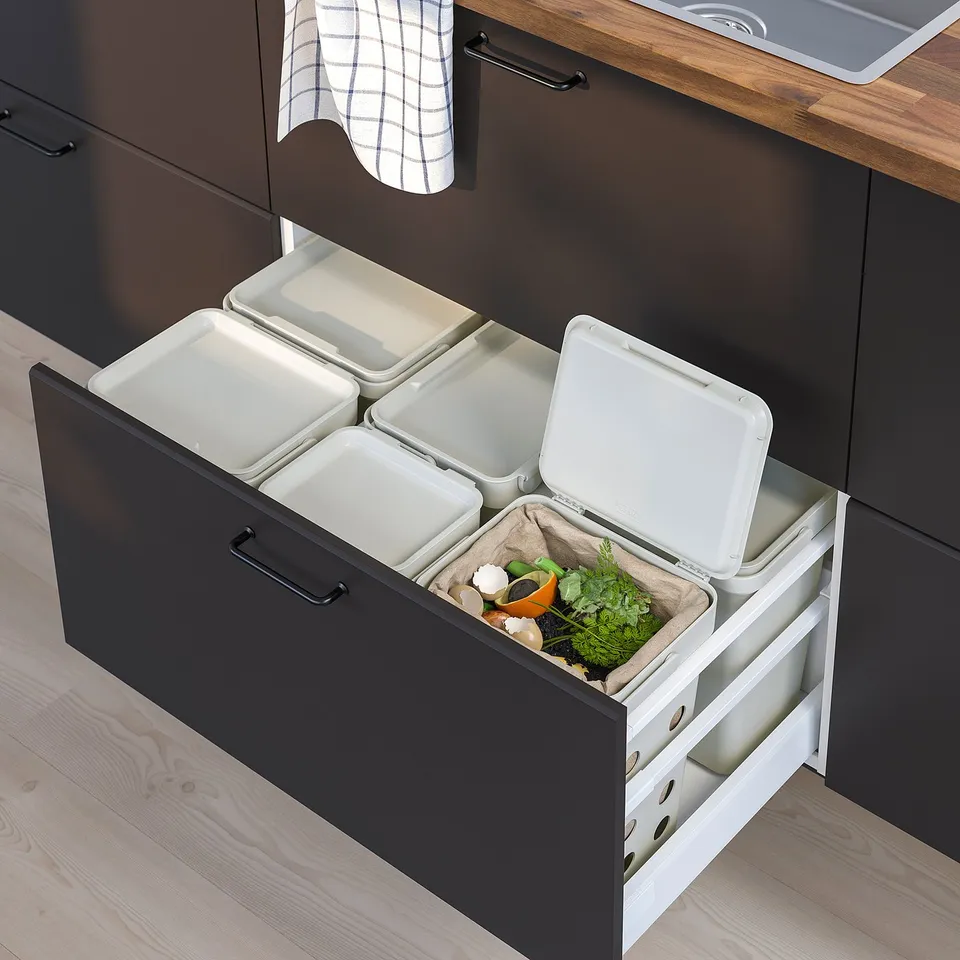Open kitchen drawer with multiple white waste sorting bins, some with lids, containing organic waste under a counter.