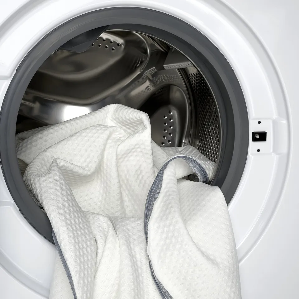 Cleaning memory foam mattress pad in white washing machine.