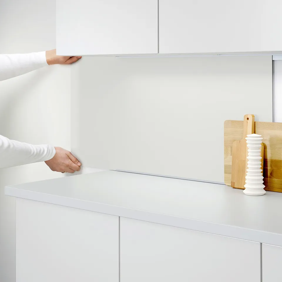 Person applying a white LYSEKIL wall panel to kitchen cabinet.