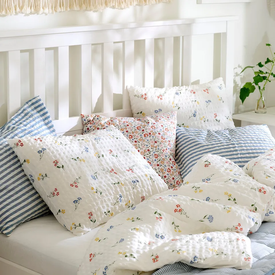 Bed with white duvet cover and pillows, featuring small colourful flower prints and seersucker texture, offering a cool, comfy, and breathable feel.