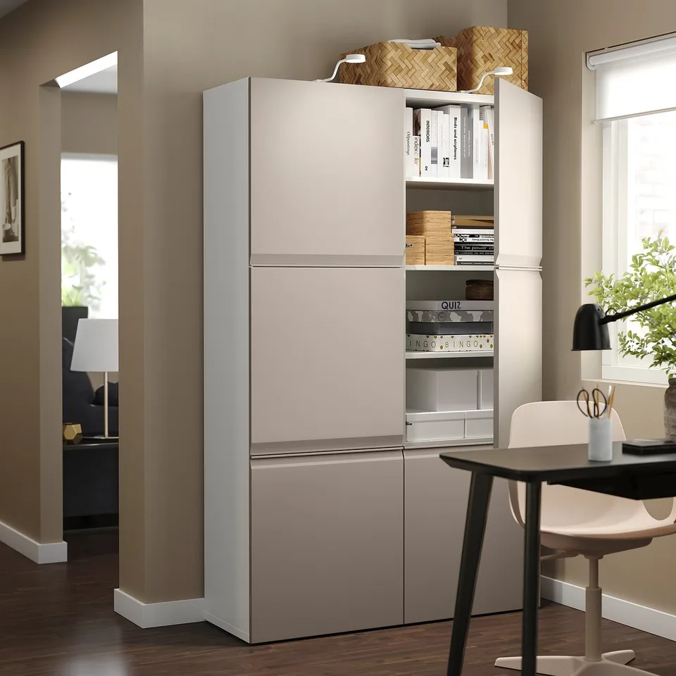 Home office with BESTÅ storage cabinet in grey, holding books and games. White chair and desk nearby, window on the right.