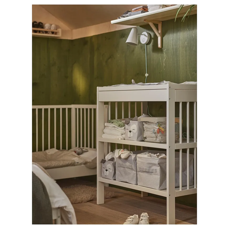 White DRÖMSLOTT nursery shelf with 3 bear bins for baby items, next to crib.
