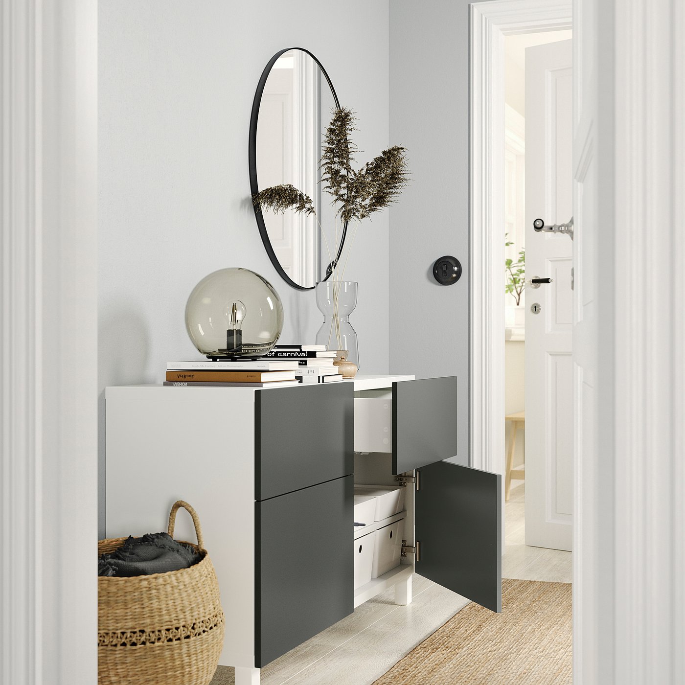 Modern hallway featuring white and black BESTÅ storage with one door open, revealing shelves and drawers. Decor includes basket, lamp, and plants.
