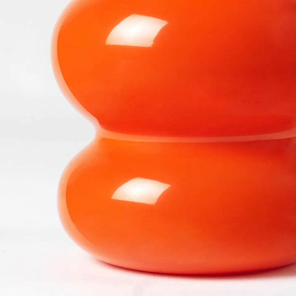 Bright orange vases, smoothly crafted, stacked neatly, reflective surface.