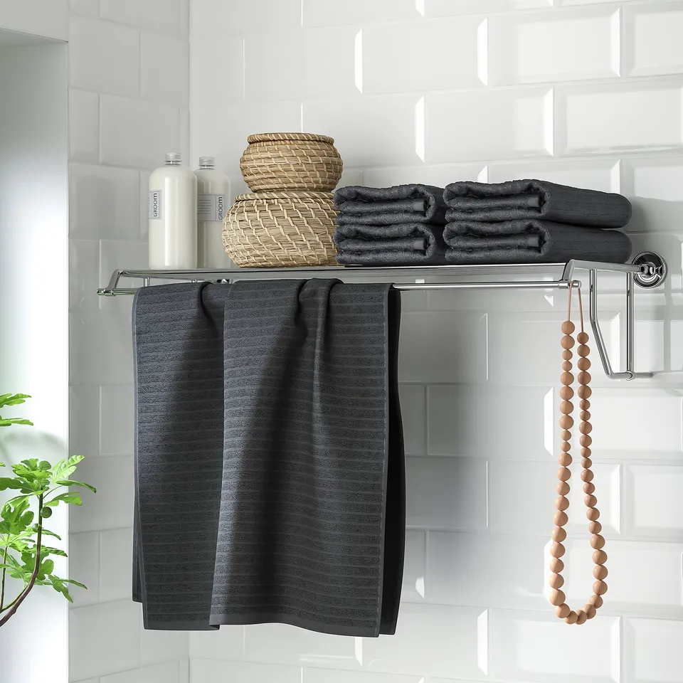 A modern bathroom shelf with towel rail and chrome-plated fixings holds dark towels neatly on tiled wall.
