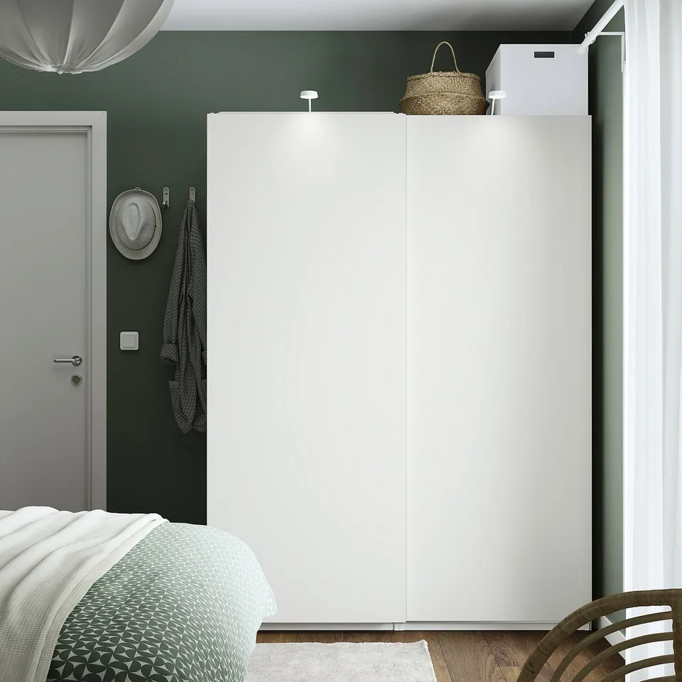 Modern bedroom with large white PAX wardrobe, green walls, grey bed, hanging hat, chair, and basket on top.