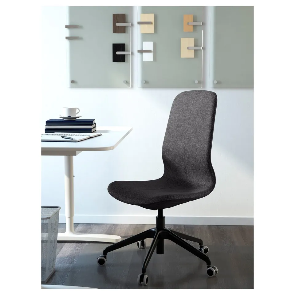 Modern grey office chair with wheels in front of desk with books and teacup.