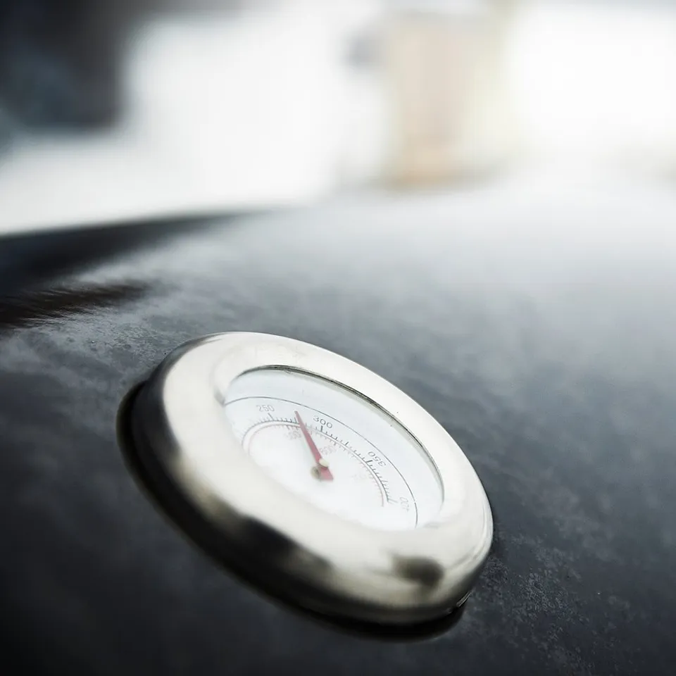 A chrome thermometer on a black metal grill, monitoring temperature during cooking.