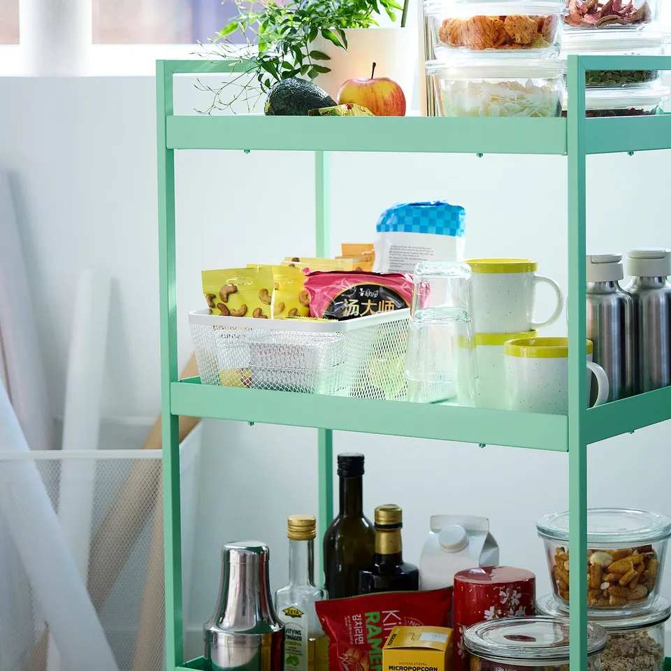 Green IKEA 365+ shelf with snacks, mugs, jars, and bottles in a mesh basket.
