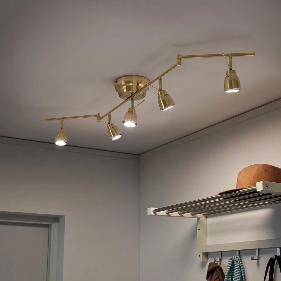 Ceiling track light with adjustable brass arms, five spots directed at different angles, mounted on white ceiling.