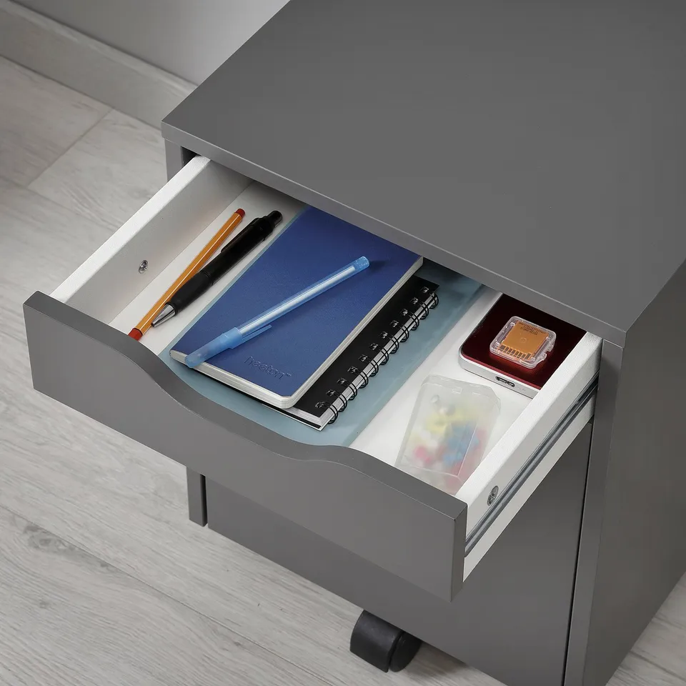Open grey drawer unit with pens, notebook, and seals, ideal for organising office supplies.