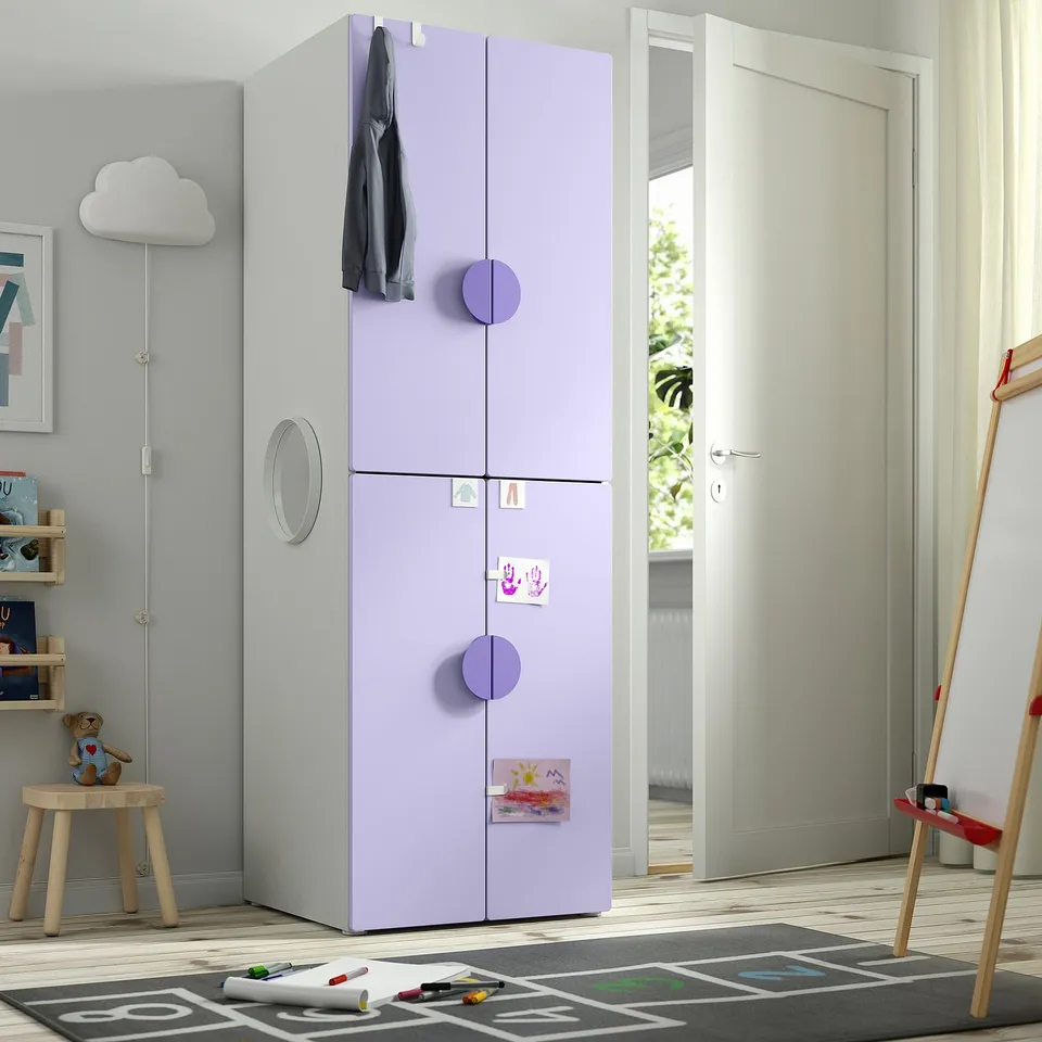 A tall, light purple SMÅSTAD wardrobe for a kid's room with two doors, circular handles, and a clothes rail on top, standing near a door.