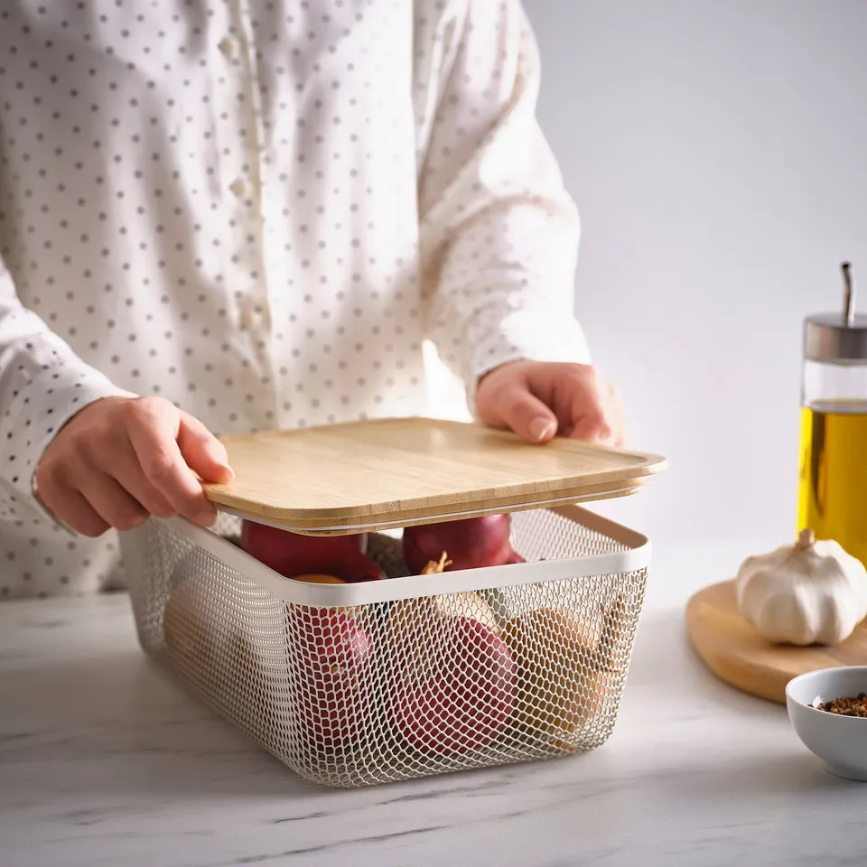 A person opening a mesh IKEA 365+ storage basket revealing stored fruits, promoting air circulation.