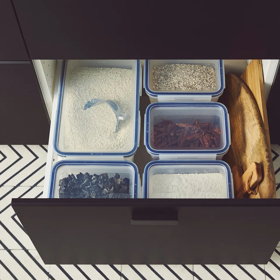 Five clear, blue-lidded IKEA 365+ containers hold different grains and dried foods in an organised drawer, with snap-lock lids for secure storage.