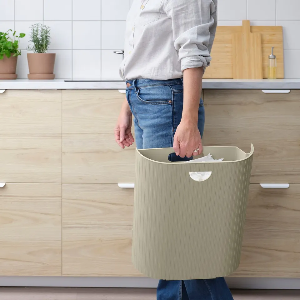 Person holding beige GÅRDSBUTIK recycling bin with handle, showing easy removal from wall bracket in kitchen.