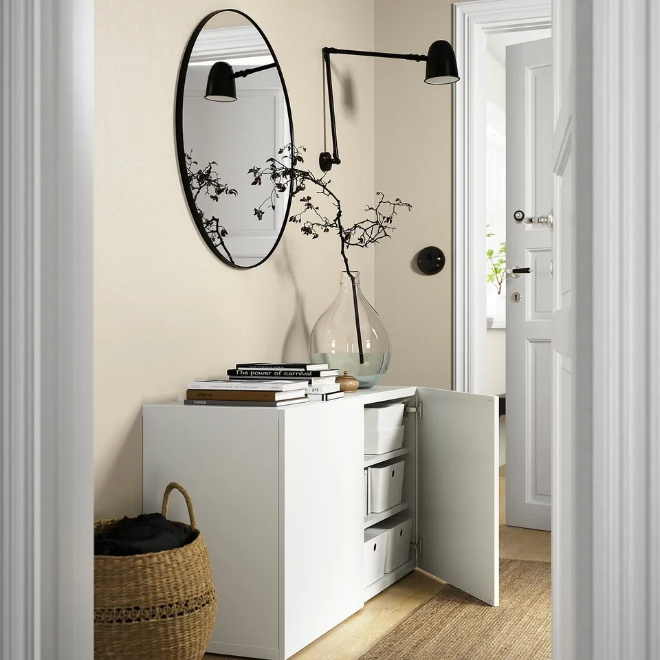 Modern storage unit with open drawer, mirror, books, vase, and light fixture.