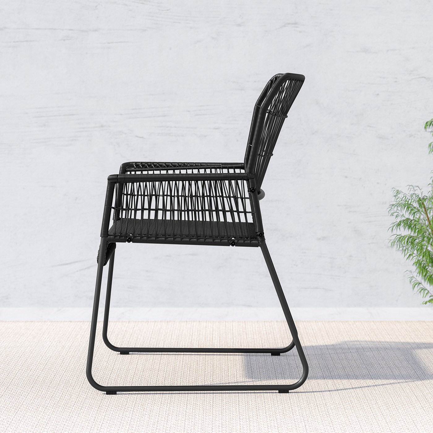 Black wicker chair, outdoor, rattan weave, comfortable for reading/dining, wall background with greenery.