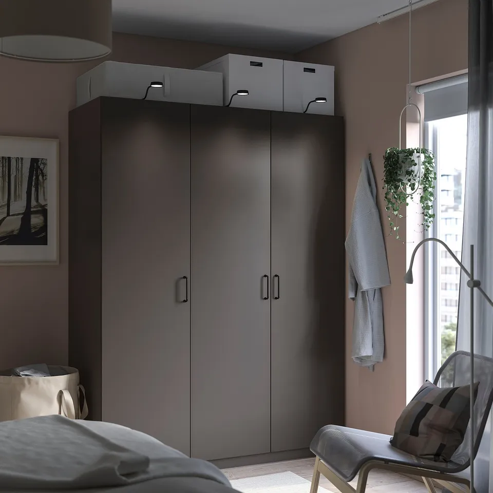 Modern bedroom with grey PAX wardrobe, white boxes, hanging clothes, chair, and window.