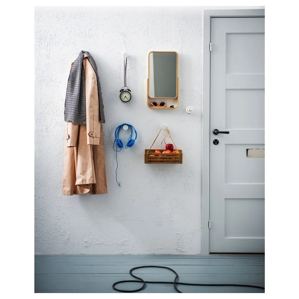 A hallway display a beige coat, blue headphones, clock, and small wooden crate of fruits next to a white door.