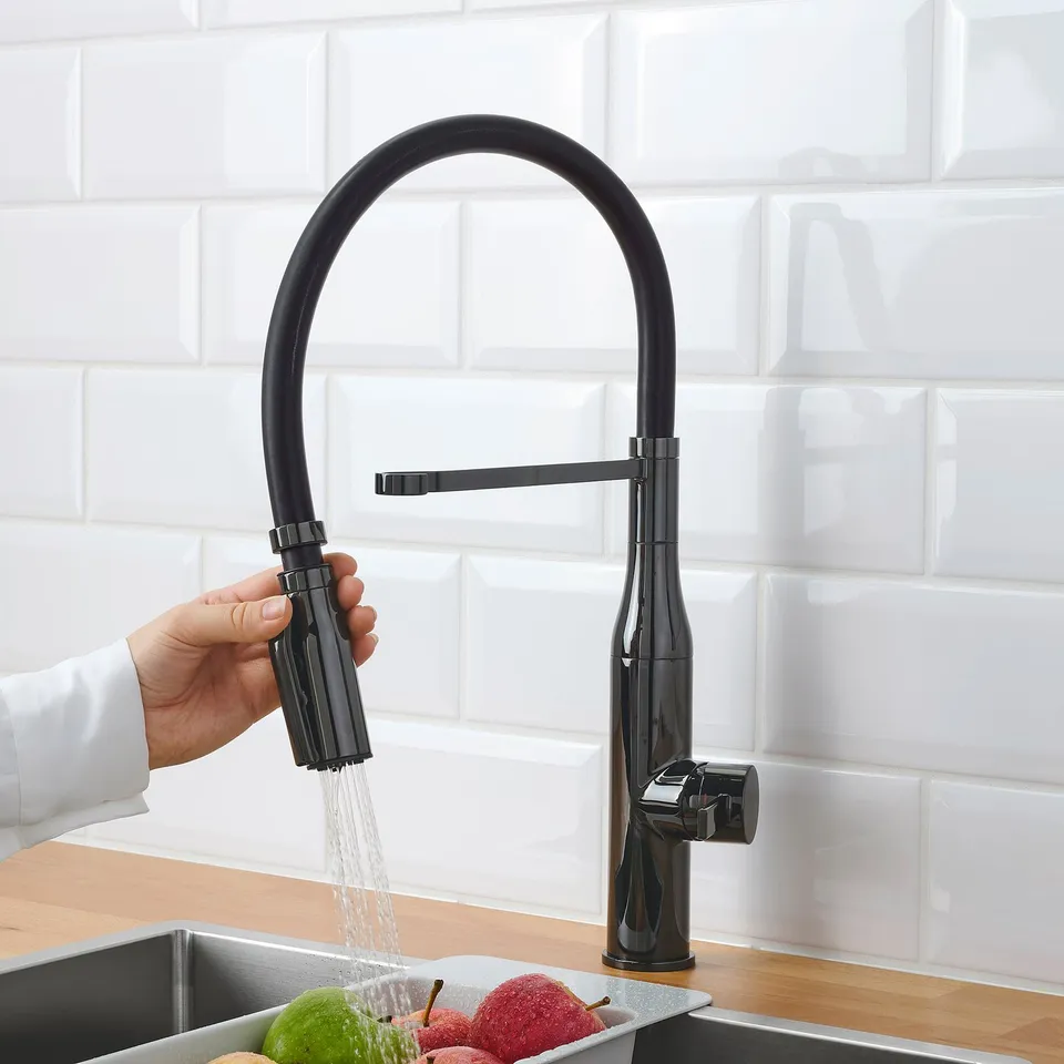 Image displays a black kitchen tap with pull-down sprayer in use, spraying water over sink and fruits.
